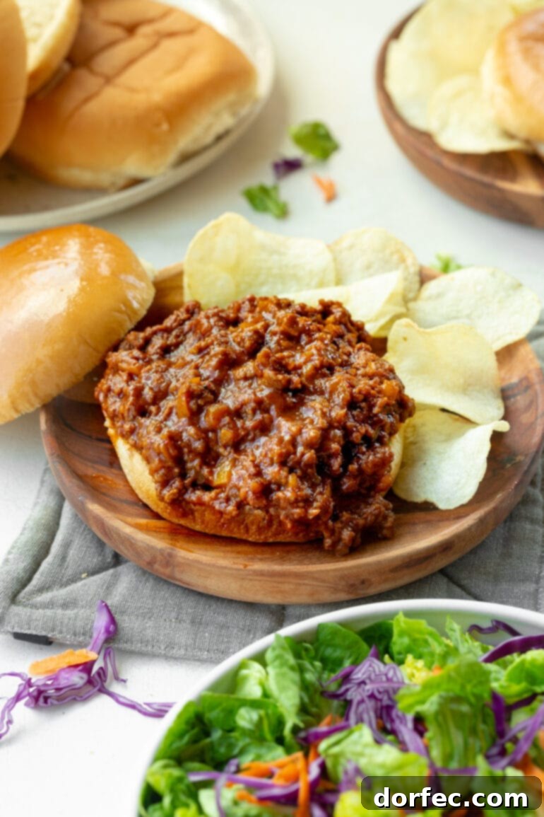 A mouthwatering homemade sloppy joe with the top bun removed, revealing the rich, saucy ground beef filling, surrounded by crisp potato chips.