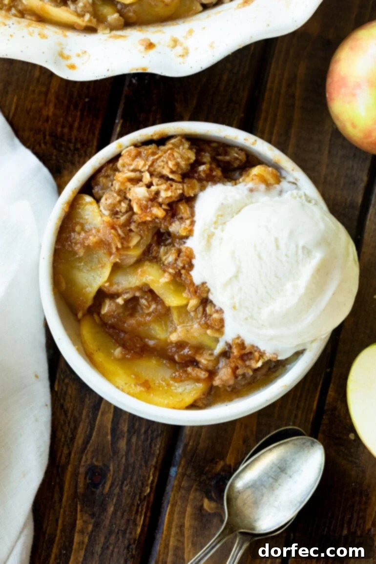 A photo of a serving of homemade apple crisp in a small bowl topped with a large scoop of vanilla ice cream, ready to be devoured.