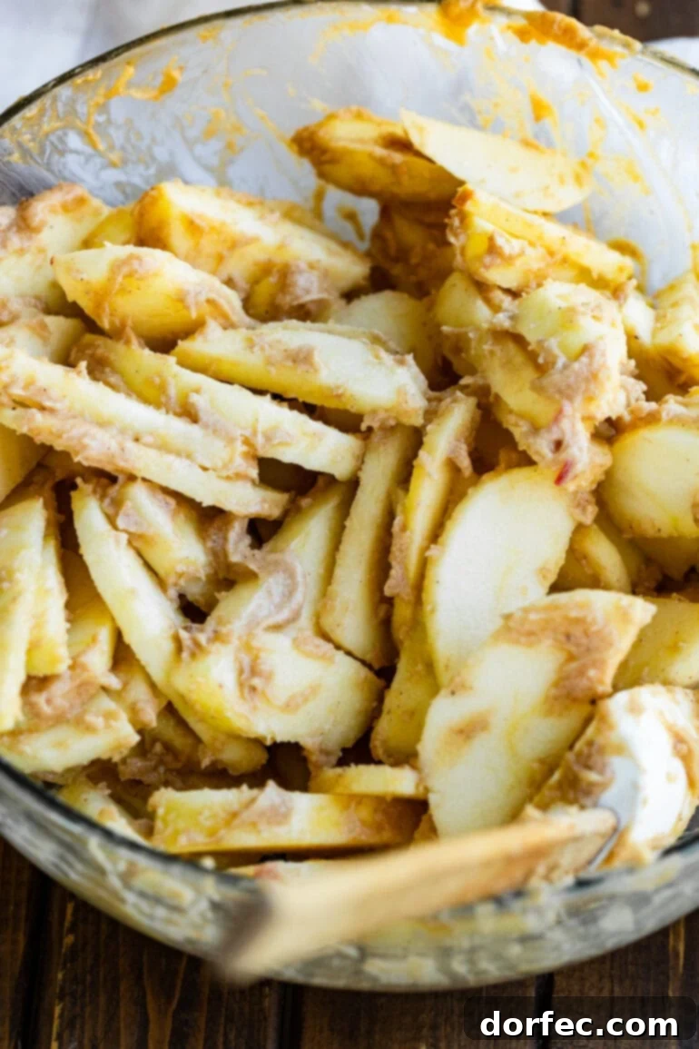 A large glass bowl full of peeled apple slices coated in a creamy sugar and cinnamon mixture ready to be baked into a homemade apple crisp.
