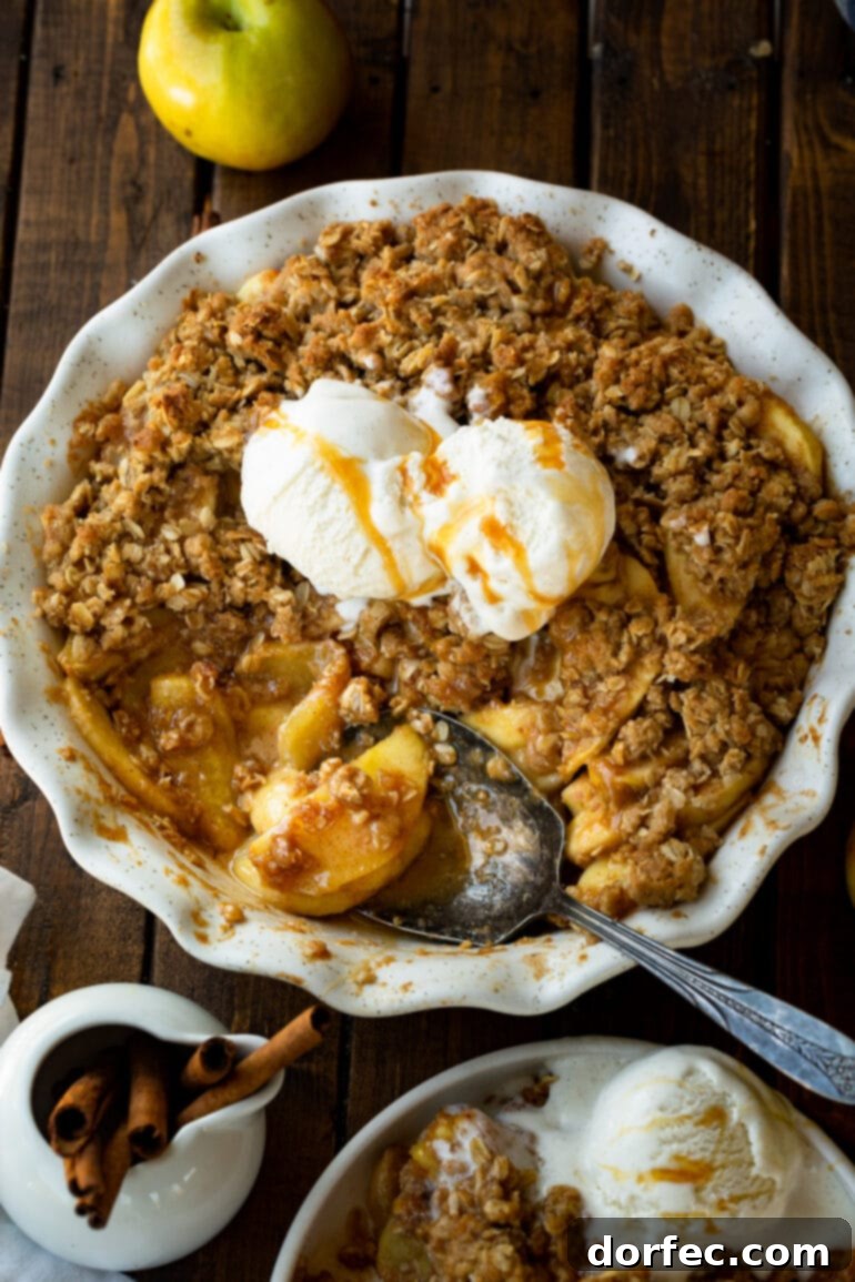 A photo of a large serving spoon scooping out a serving of warm apple crisp topped with scoops of vanilla ice cream, perfectly capturing the indulgent moment.