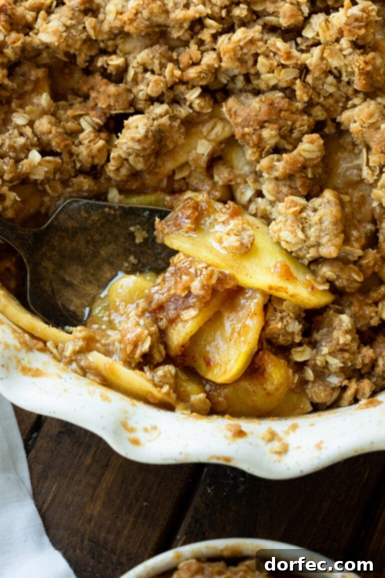 A close-up photo of a homemade apple crisp with a scoop removed, revealing the tender, spiced apples and the buttery, crumbly topping inside.