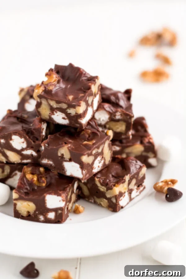 Several squares of homemade Rocky Road Fudge stacked on a small white dessert plate, perfect for holidays.