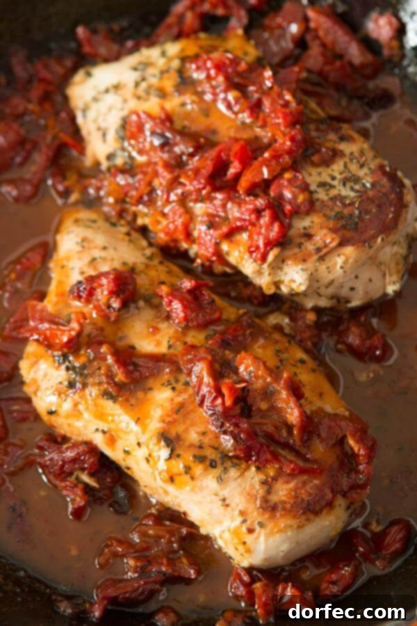 A close-up shot of cooked chicken breasts topped with vibrant sun-dried tomatoes, glistening in a savory sauce.