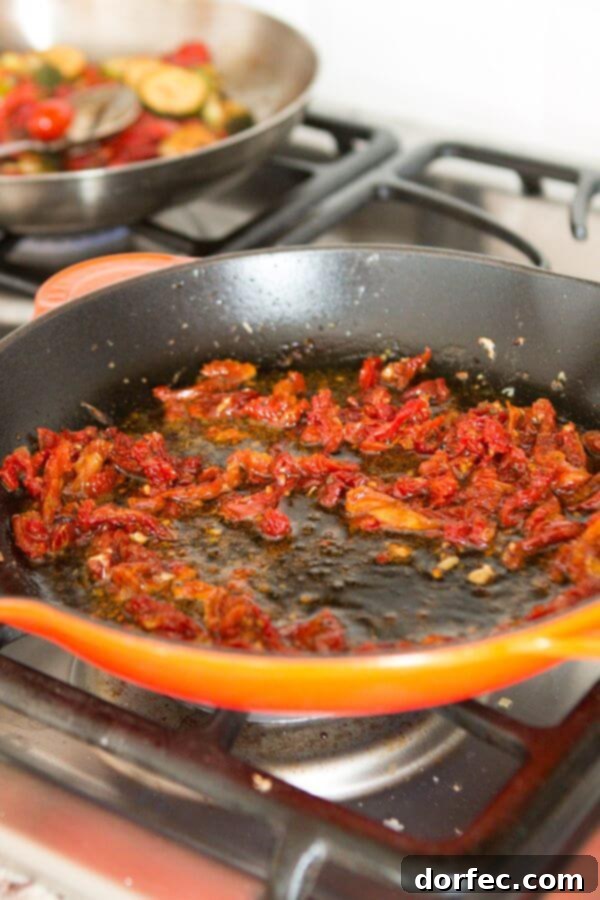Sun-dried tomatoes simmering enticingly in a cast iron skillet with bright orange juice, forming the base of a rich sauce.