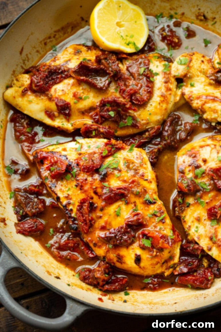 Cooked golden chicken breasts topped with sun-dried tomatoes, resting in flavorful cooking juices within a shallow Dutch oven.