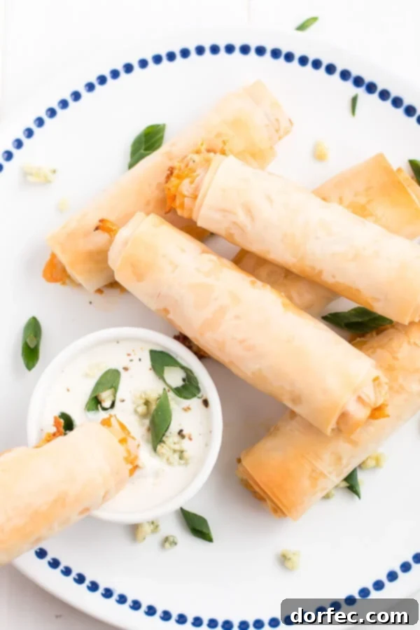 Crispy, flaky, creamy, spicy... these Buffalo Chicken Phyllo Rolls have it all! A plate of freshly baked Buffalo Chicken Phyllo Rolls, garnished with green onions and ready for dipping.