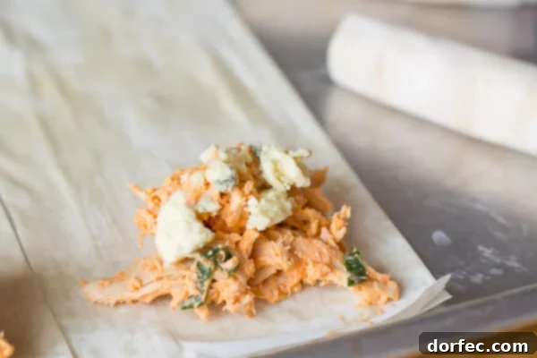 Crispy, flaky, creamy, spicy... these Buffalo Chicken Phyllo Rolls have it all! A single Buffalo Chicken Phyllo Roll, perfectly golden and showing its inviting layers, next to a bowl of blue cheese dressing.