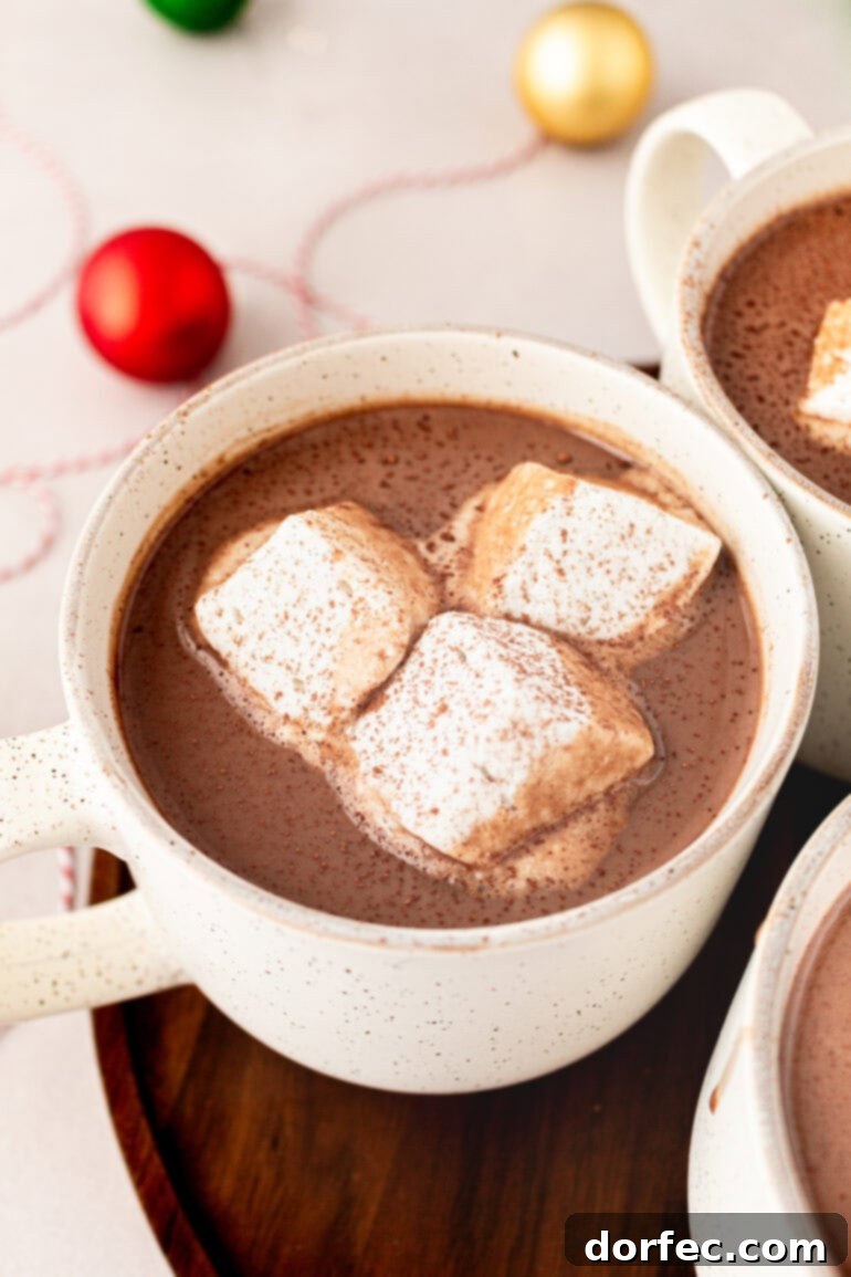 Velvety Homemade Hot Chocolate Perfection 10 A close-up of a white mug filled to the brim with creamy homemade hot chocolate, elegantly topped with three large, fluffy marshmallows, offering a luxurious treat.