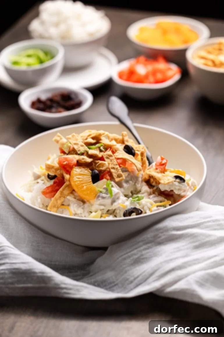 Creamy coconut milk chicken sauce draped over a bed of fluffy white rice in a pristine white bowl, adorned with a colorful medley of fresh toppings like pineapple, cheddar cheese, and green onions.