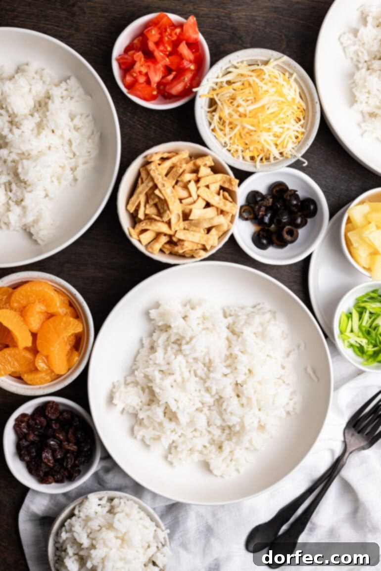 A beautifully arranged spread of fresh Hawaiian Haystacks ingredients, including fluffy white rice, vibrant pineapple chunks, crisp celery, juicy diced tomatoes, rich cheddar cheese, bright green onions, and golden crispy wonton strips, all ready for assembly.