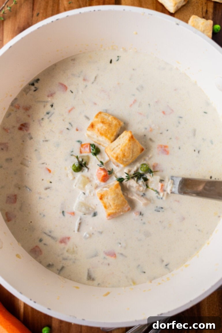 A photo of a bowl of creamy chicken pot pie soup topped with mini biscuits with a spoon sitting in the bowl