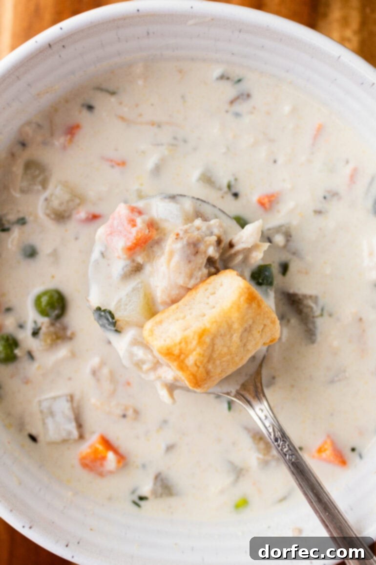 A photo of a spoonful of creamy chicken pot pie soup being lifted from a full bowl with a little biscuit on top