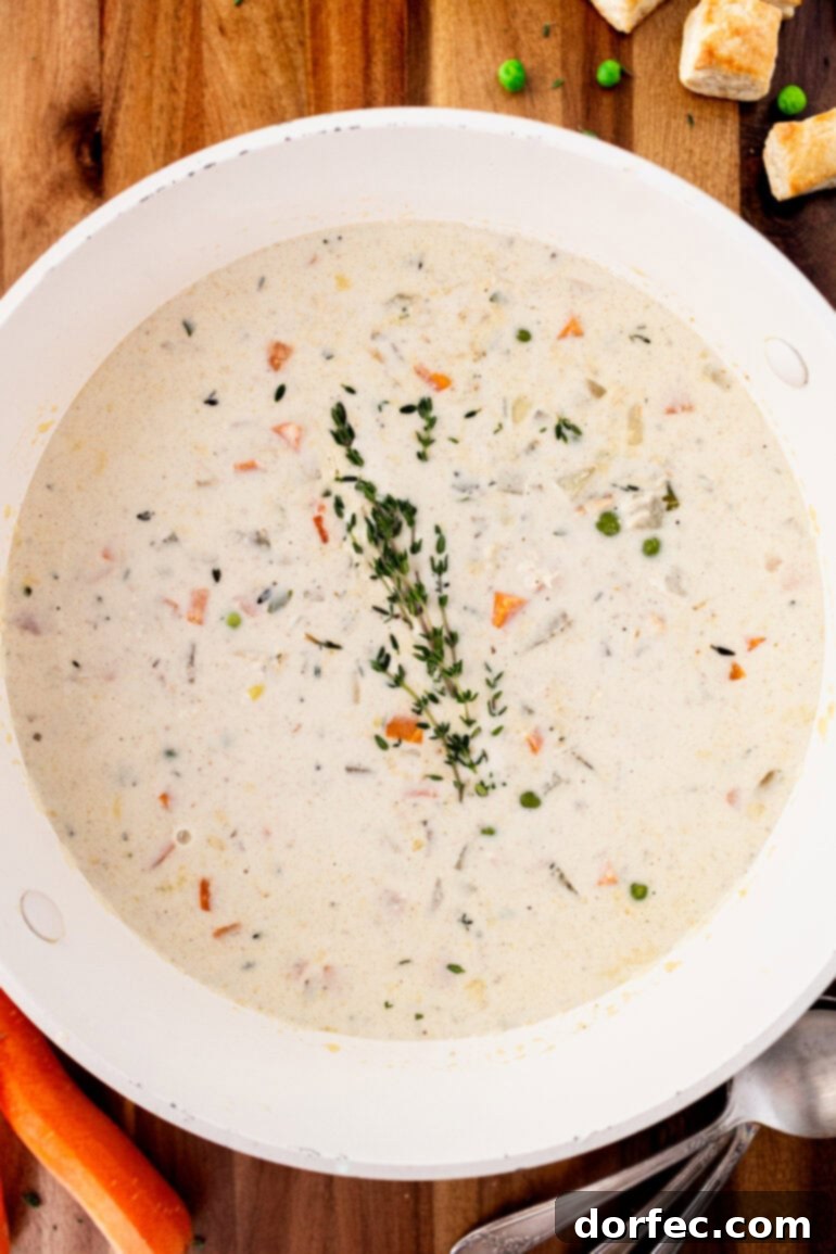 A photo of a large white bowl of creamy chicken pot pie soup sprinkled with fresh herbs
