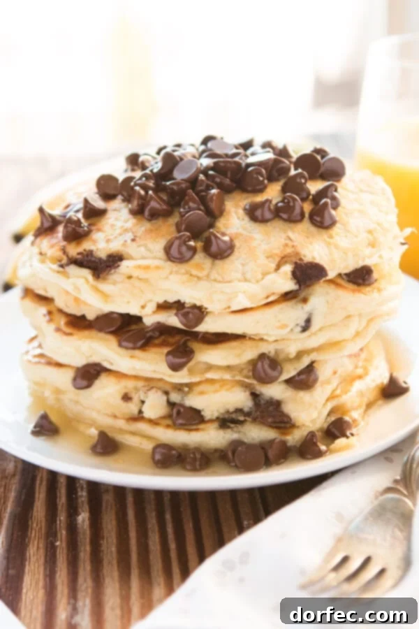 A beautifully arranged stack of chocolate chip pancakes on a white plate, accompanied by a fork and napkin, inviting you to dig in.