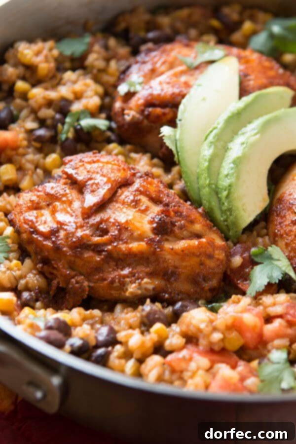 Close-up of a Mexican Fiesta Chicken and Rice skillet, showing chicken, rice, corn, and black beans, with avocado slices
