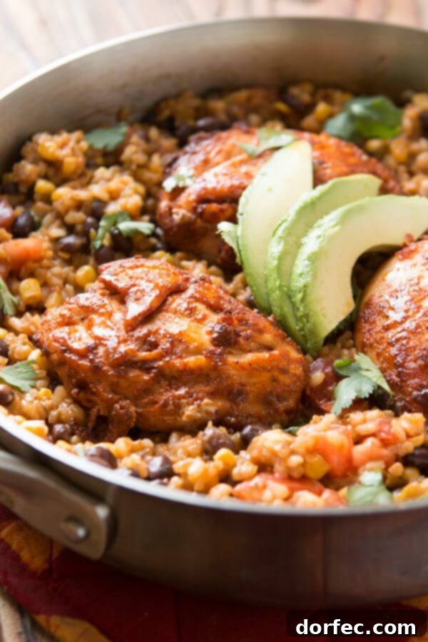 Mexican chicken and rice skillet with melted cheese, black beans, corn, and tomatoes, topped with fresh avocado slices.