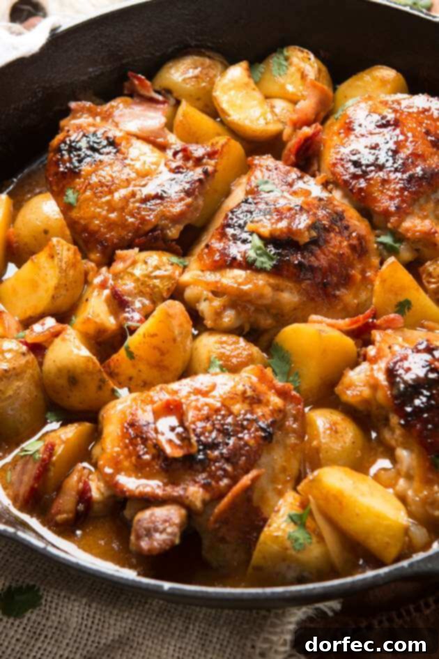A close-up of perfectly braised Dijon chicken thighs and tender Yukon gold potatoes, glistening with sauce in a cast iron pan.
