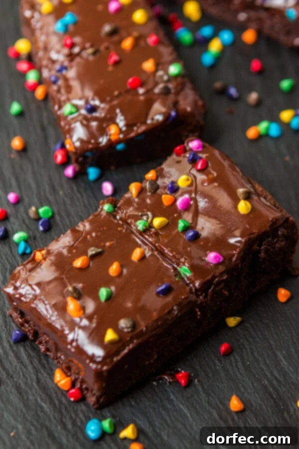 A close-up shot of a perfectly fudgy Cosmic Brownie, sliced and ready to eat, topped with chocolate ganache and rainbow candies.