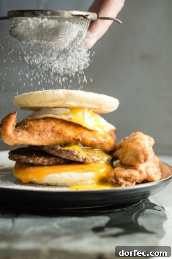 A stacked fried chicken and sausage breakfast sandwich, featuring crispy fried chicken, savory sausage, and fluffy pancakes.