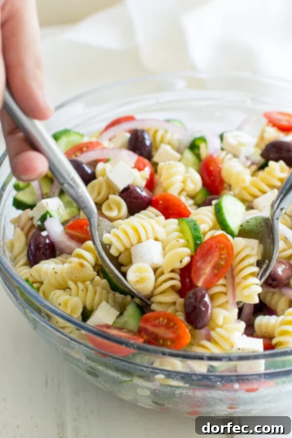 Easy Greek Pasta Salad 12 Two serving spoons scooping a generous portion of Greek Pasta Salad from a large bowl, ready to be served.