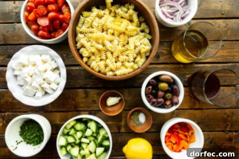 Easy Greek Pasta Salad 3 A flat lay photograph showcasing all the fresh ingredients for Greek pasta salad, neatly arranged in separate small bowls, including pasta, diced vegetables, feta, and olives.