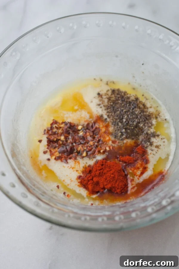 A glass bowl filled with the vibrant ingredients for garlic parmesan wing sauce, featuring melted butter, grated parmesan, and various spices.