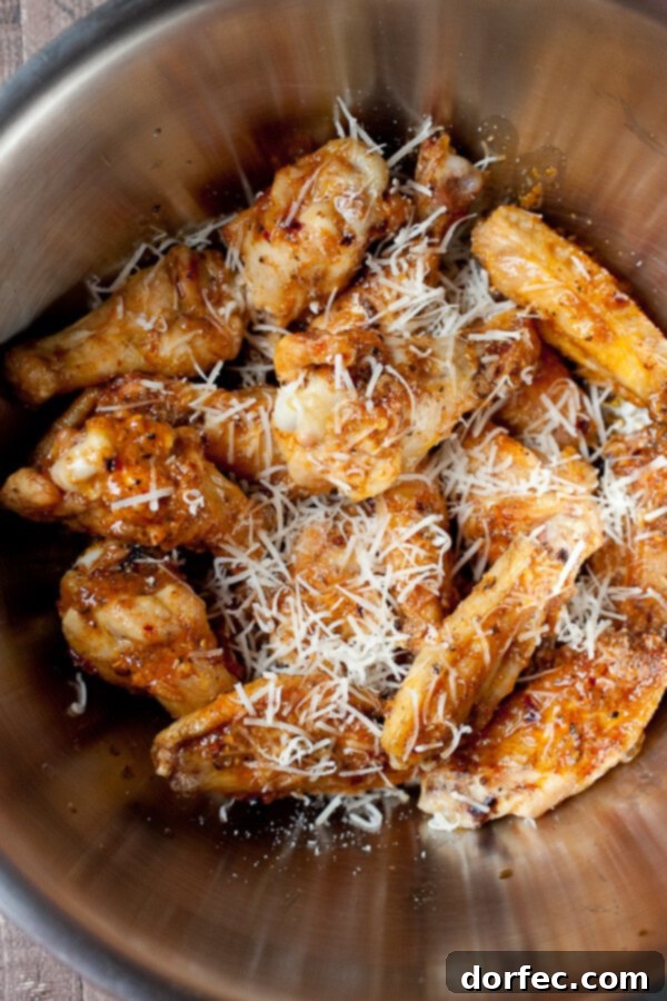 Grilled chicken wings being generously tossed in a rich garlic parmesan wing sauce, ensuring every piece is coated in flavor.