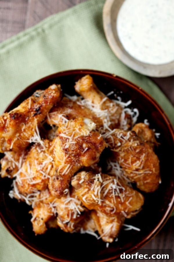 A generous pile of crispy, golden-brown garlic parmesan grilled chicken wings, glistening with sauce and ready to be served, on a white plate.