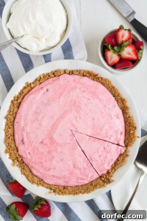 A slice of creamy Strawberry Icebox Pie with a pretzel crust, topped with whipped cream and fresh strawberries.