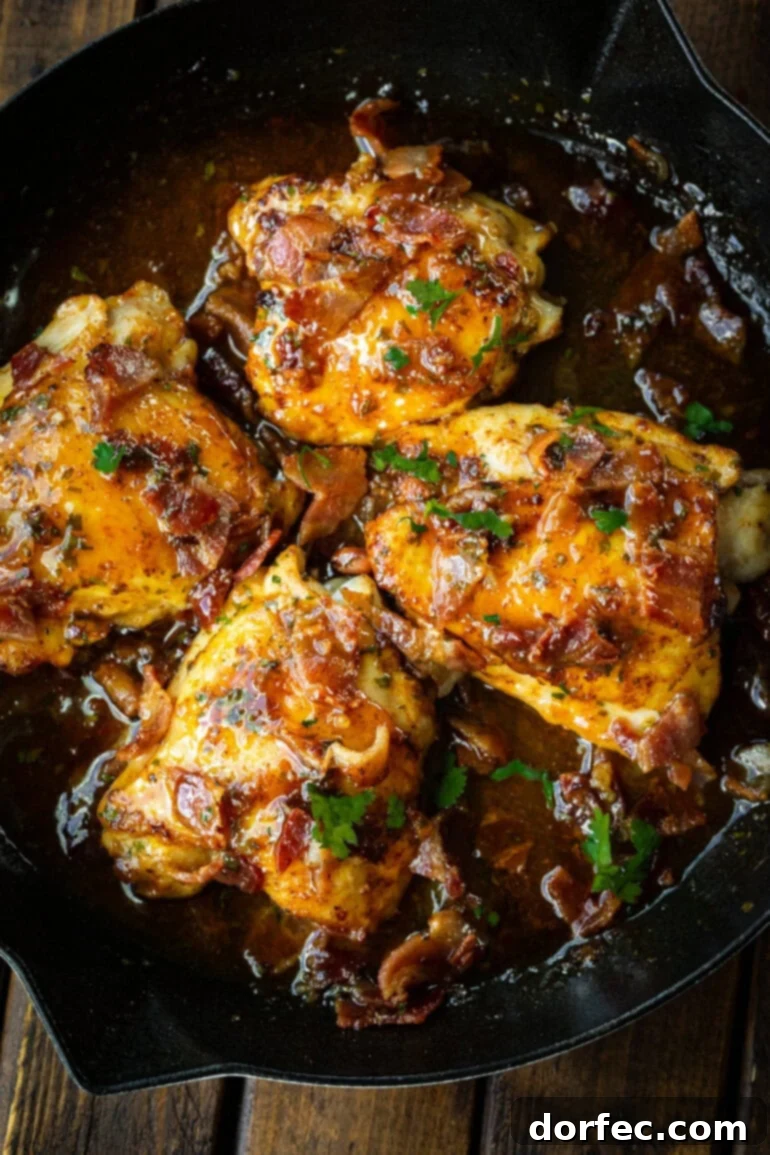 A photo of four golden pan-seared chicken thighs swimming in a rich honey mustard sauce, topped with crumbled bacon and fresh cilantro, in a cast iron skillet.