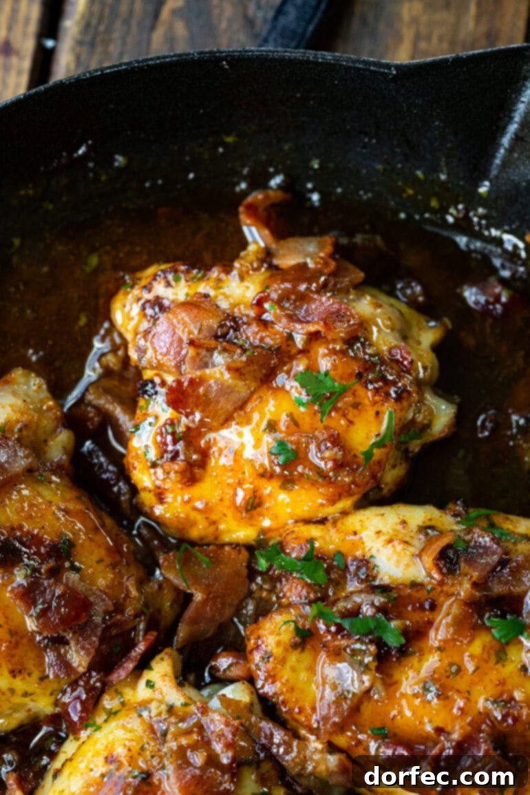 A close-up photo of a golden chicken thigh resting in a rich, glistening honey mustard sauce in a cast iron skillet, ready to be served.