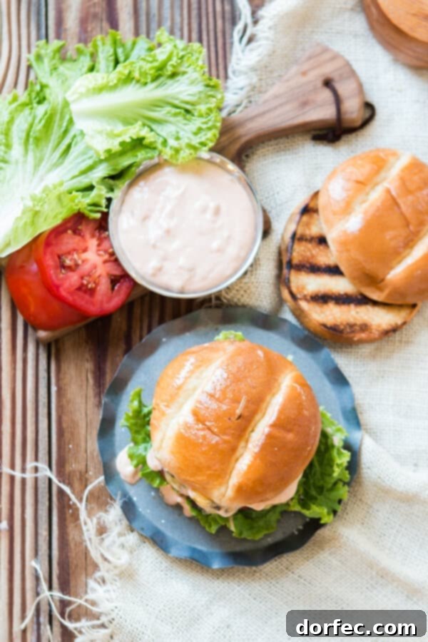 This is it, the killer burger sauce recipe. If you don't want dry, stale burgers look no further for the best classic hamburger sauce. An overhead view of a perfectly assembled cheeseburger, sauce generously dripping, alongside a toasted brioche bun, a small bowl of sauce, and thinly sliced tomatoes.