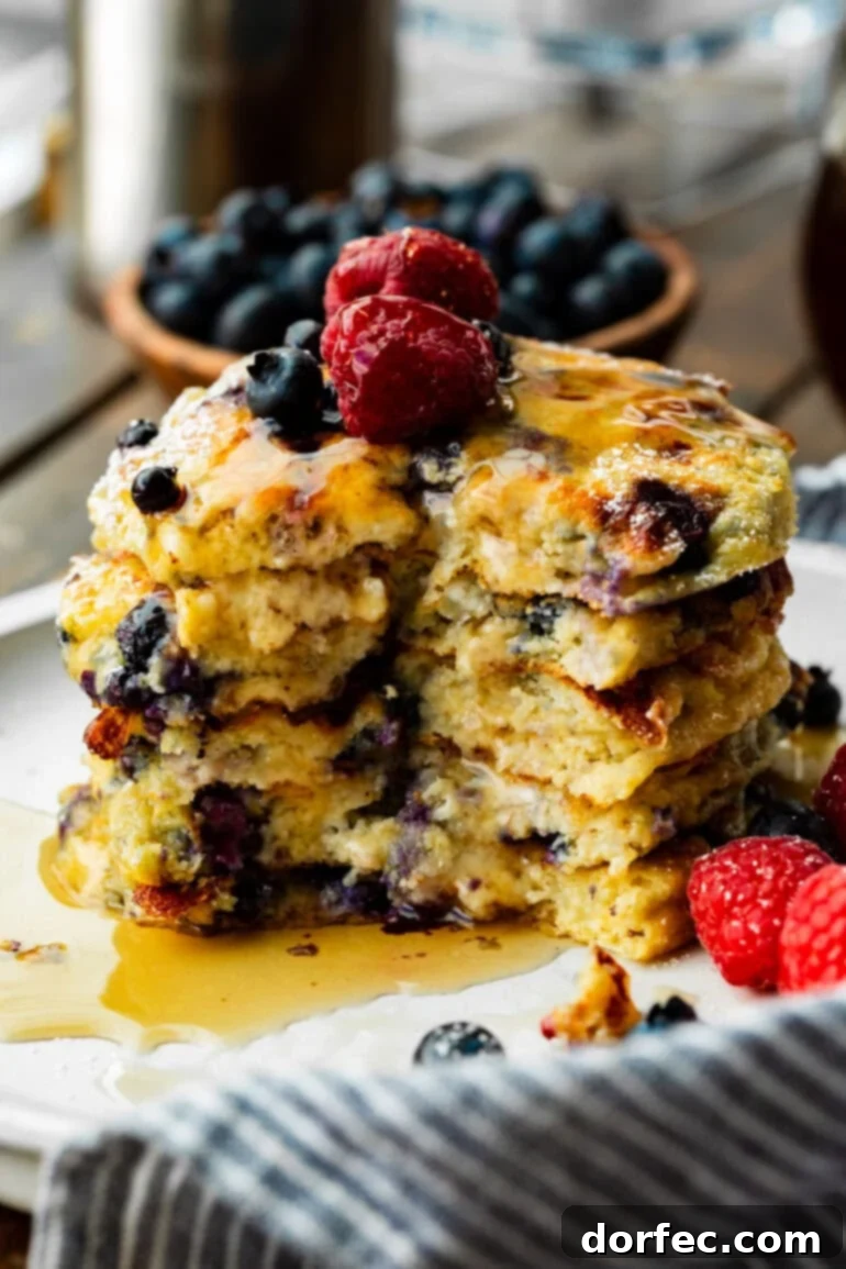 A tall stack of five fluffy blueberry pancakes with a bite taken out, generously topped with fresh berries and maple syrup, inviting you to enjoy a healthy and delicious breakfast.
