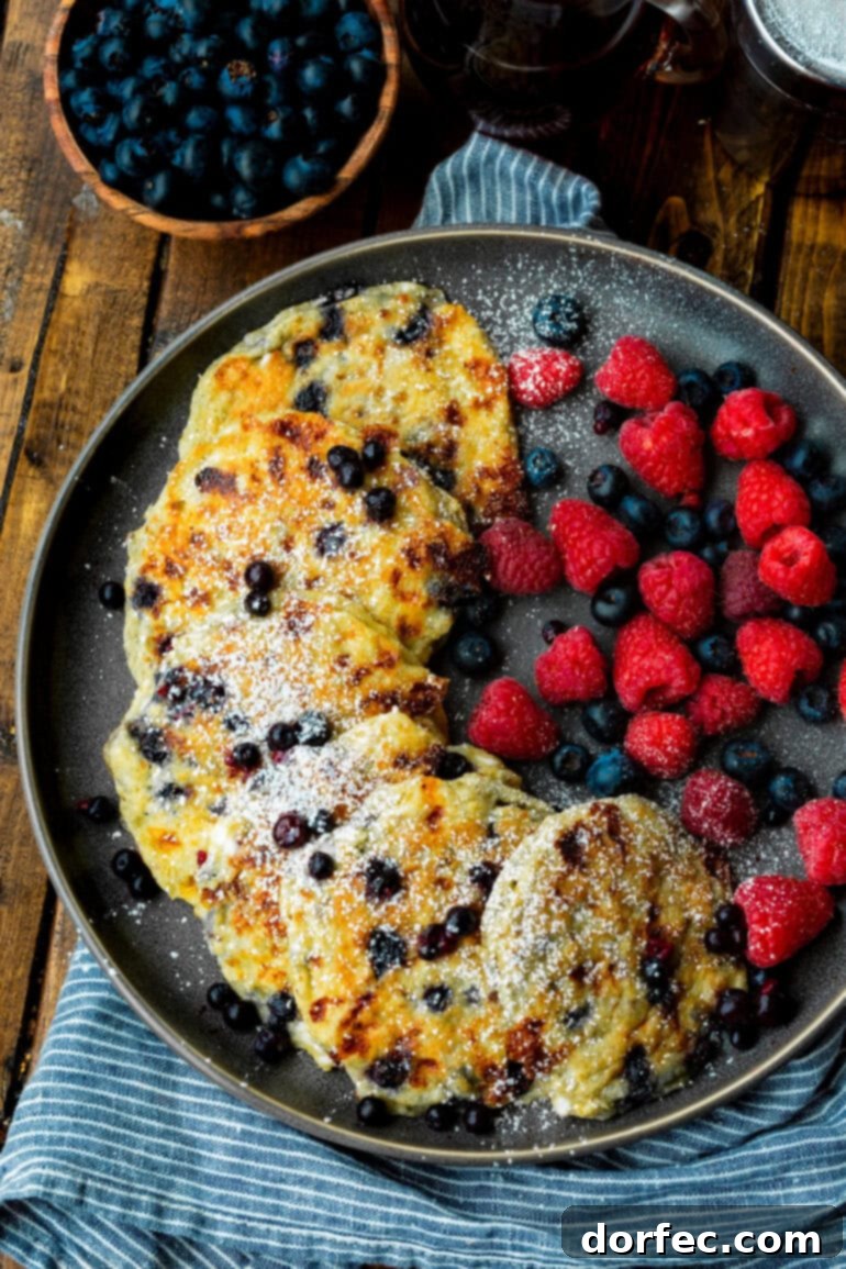 A stunning plate featuring several golden blueberry cottage cheese pancakes, elegantly arranged with a scattering of fresh blueberries and raspberries on the side.