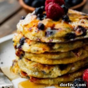 A photo of a stack of blueberry cottage cheese pancakes covered in maple syrup and topped with fresh raspberries and blueberries