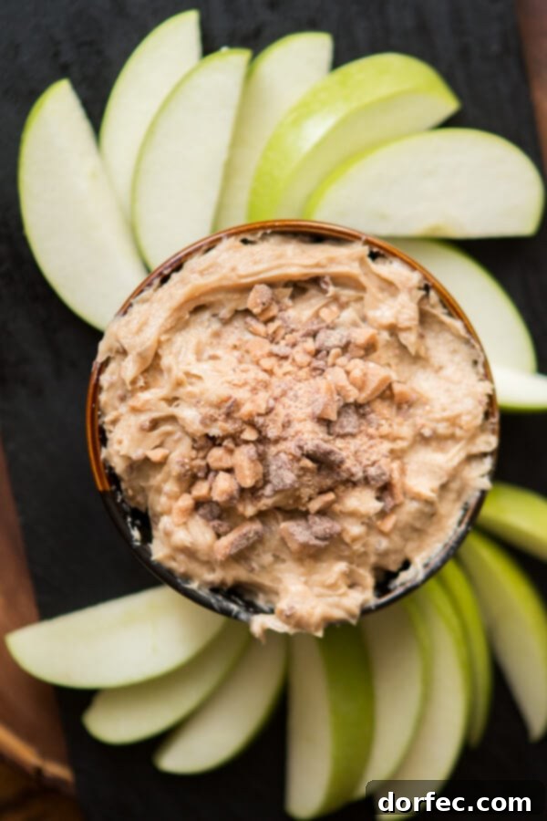 A close-up shot of creamy toffee apple dip, showcasing its smooth texture and visible pieces of milk chocolate toffee, with fresh apple slices arranged artfully around it, inviting a delicious scoop.