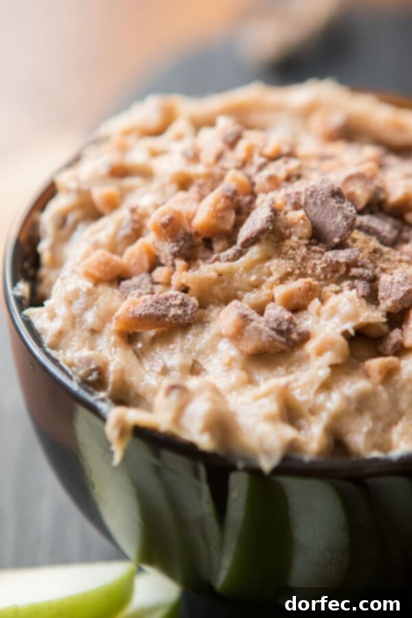 A spoonful of rich, creamy Toffee Apple Dip being scooped from a bowl, highlighting its luscious texture, with blurred fresh apple slices in the background, ready for dipping.