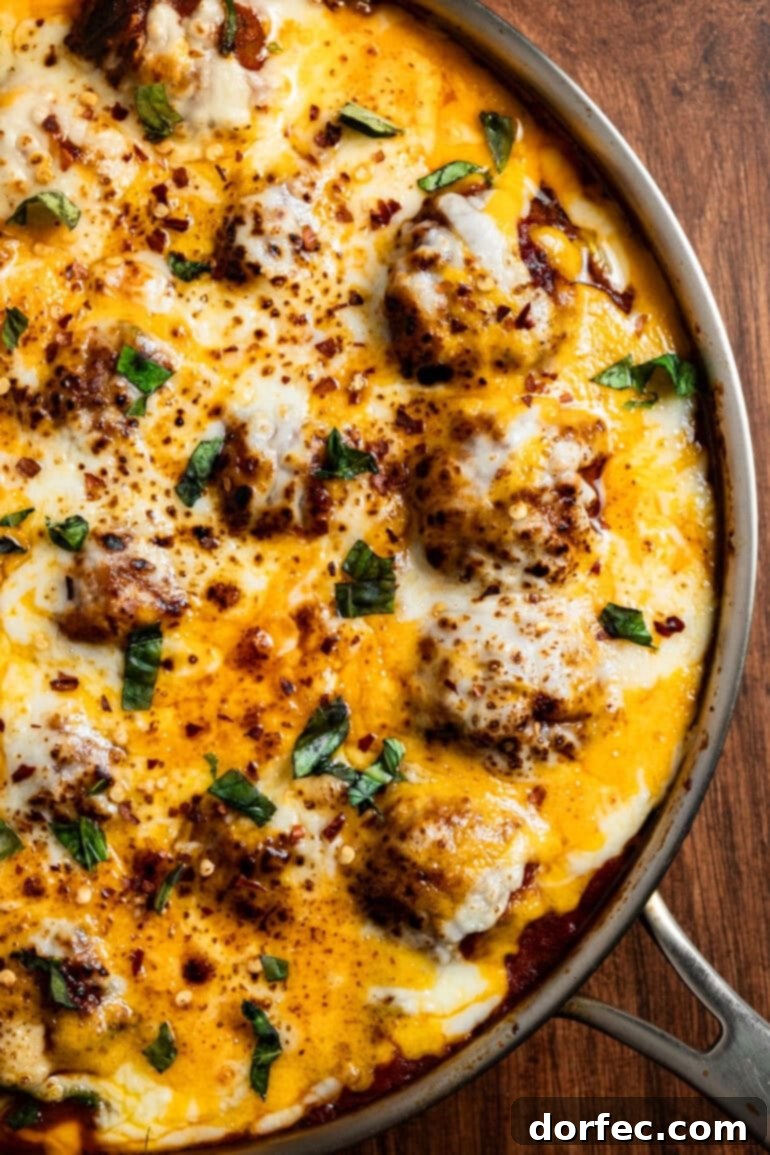 Hearty Cheesy Meatball and Zucchini Skillet 3 a photo taken over the top of a skillet full of meatballs sitting in a marinara sauce mixed with zoodles topped with melted cheese and chopped basil.