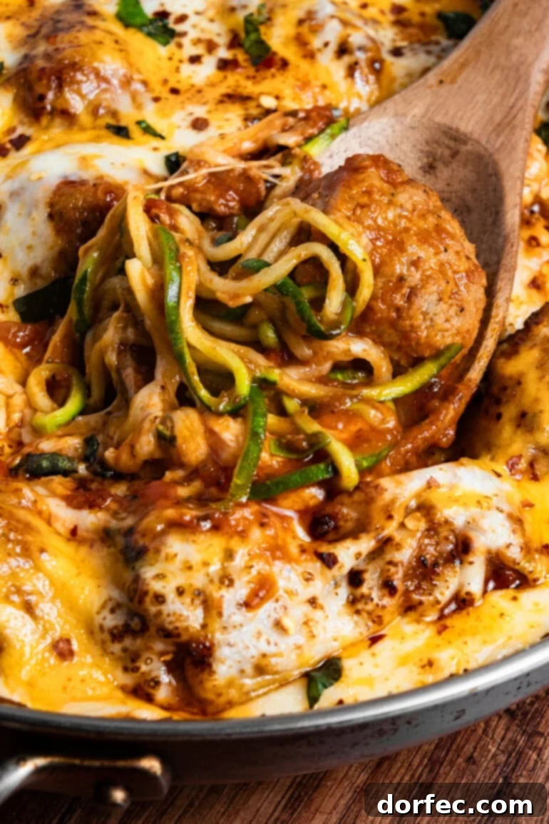 Hearty Cheesy Meatball and Zucchini Skillet 4 a close up photo of meatball sitting in marinara sauce in a skillet and pile of zoodles sitting on top
