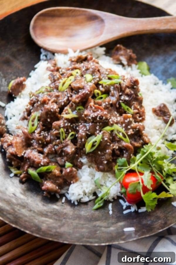 A bowl of Slow Cooker Korean BBQ Beef served with rice and fresh green onions, ready to be enjoyed.