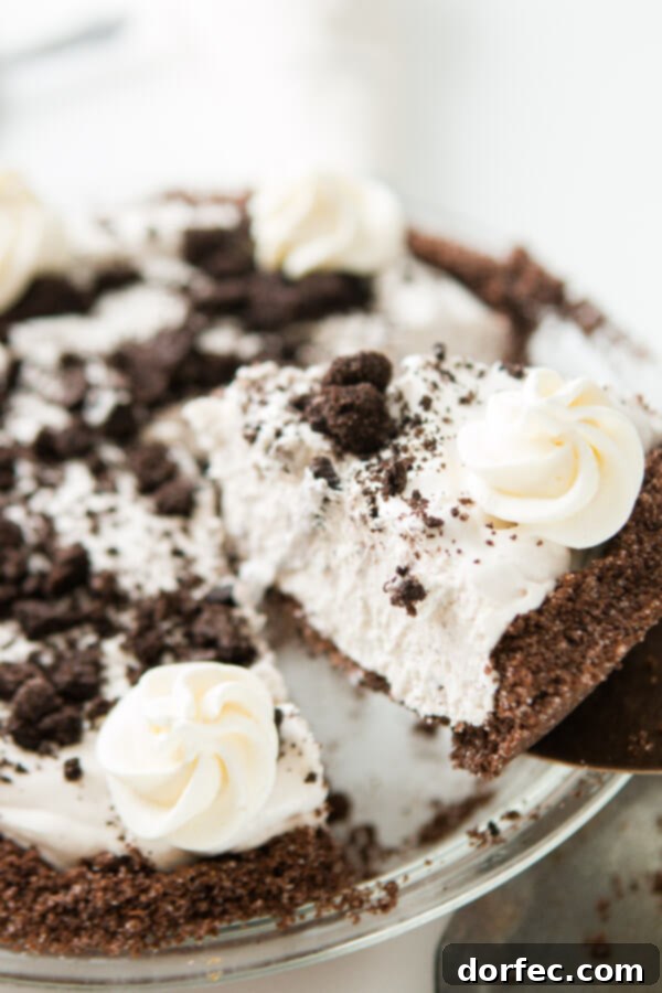 A cake knife gently lifting a piece of homemade Oreo cookie pie with its distinct chocolate graham cracker crust, ready to be served.