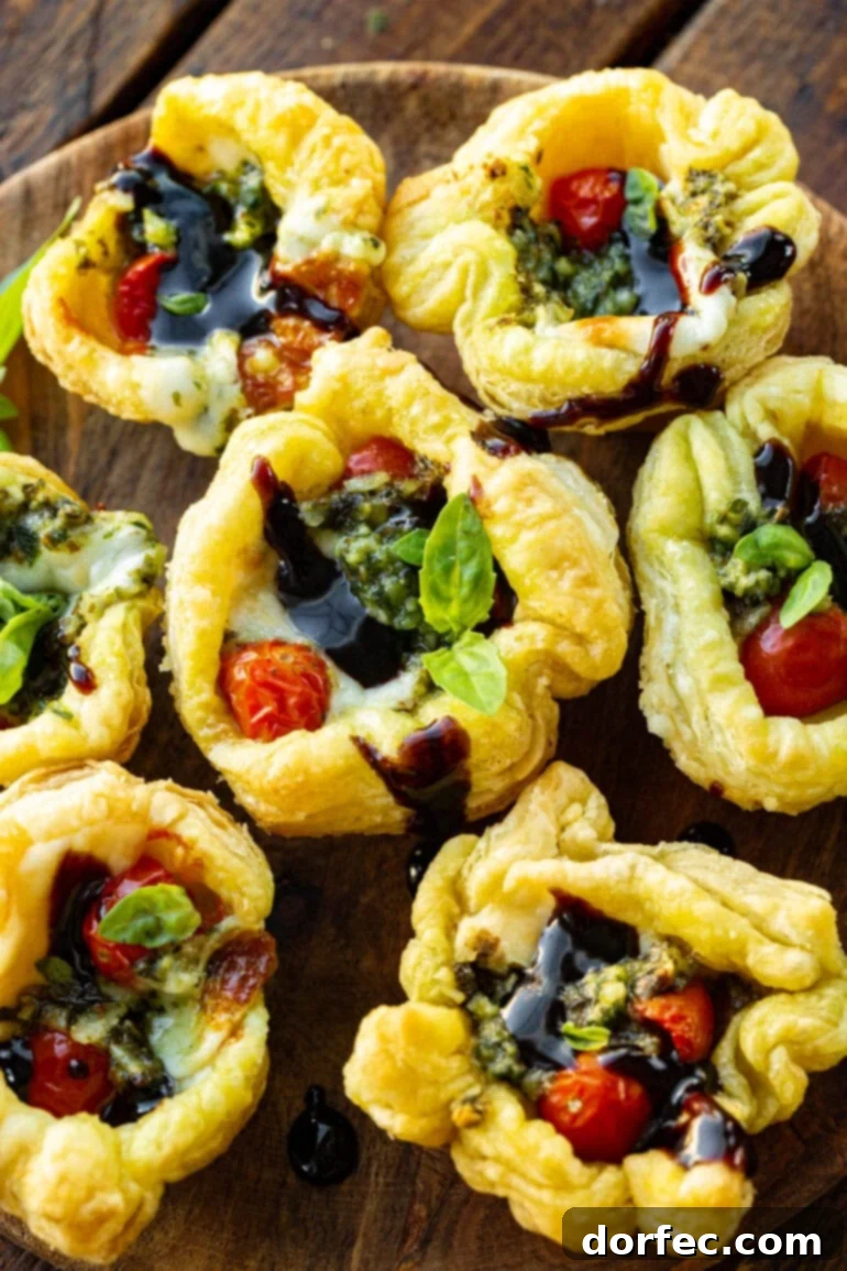 a photo of several pesto tartlets topped with balsamic glaze, basil and tomatoes