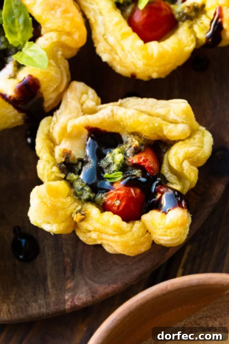a photo of a golden baked puff pastry pesto cup topped with a balsamic glaze and fresh basil.