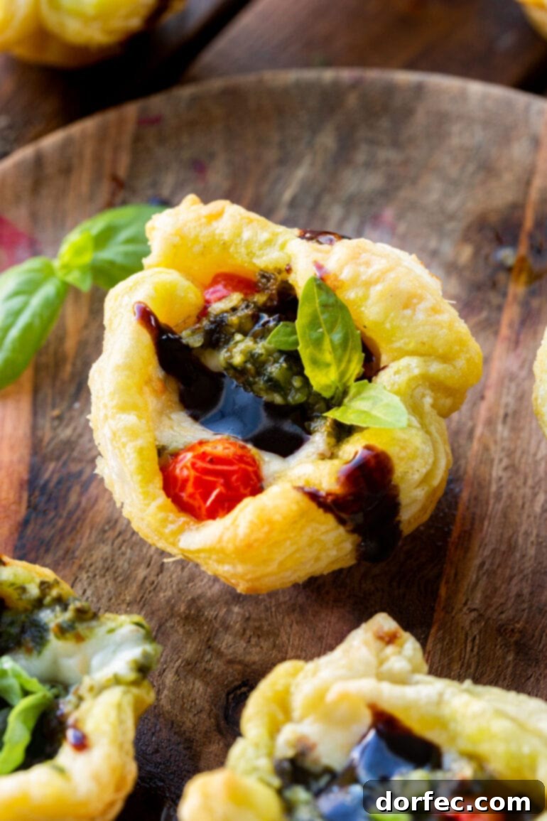 a photo of a golden baked caprese pesto tart topped with balsamic glaze and a cherry tomato.