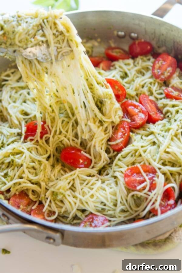 Tongs expertly pulling up a generous portion of cheesy pesto pasta from a large skillet, ready to be served, showcasing the rich, coated noodles.