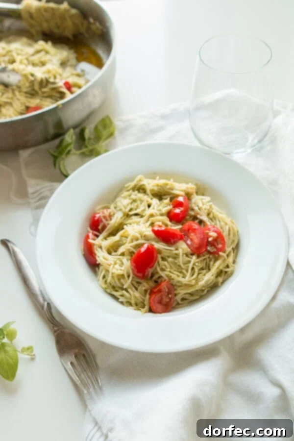 A pristine white bowl filled with basil pesto pasta, artfully placed next to a fork and a glass of water, suggesting a complete and satisfying meal.