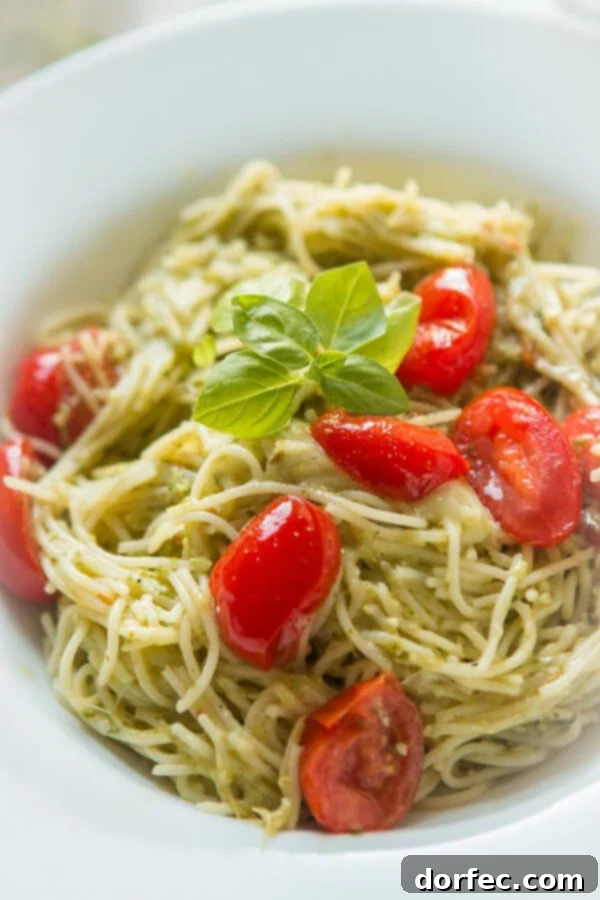 A bowl of vibrant pesto sauce pasta, beautifully garnished with fresh grape tomatoes and fragrant basil leaves, highlighting the colorful and appetizing presentation of the dish.