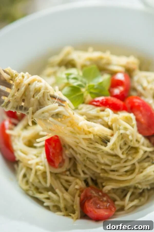 A close-up shot of a fork pulling on a generous swirl of cheesy pesto pasta, emphasizing the creamy texture and inviting appearance of the dish.