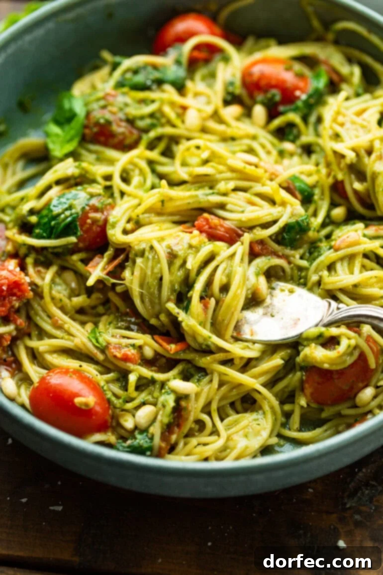 A close-up shot of a fork expertly scooping a generous portion of pesto-covered angel hair pasta from a large bowl, highlighting the creamy texture and vibrant colors of the dish.