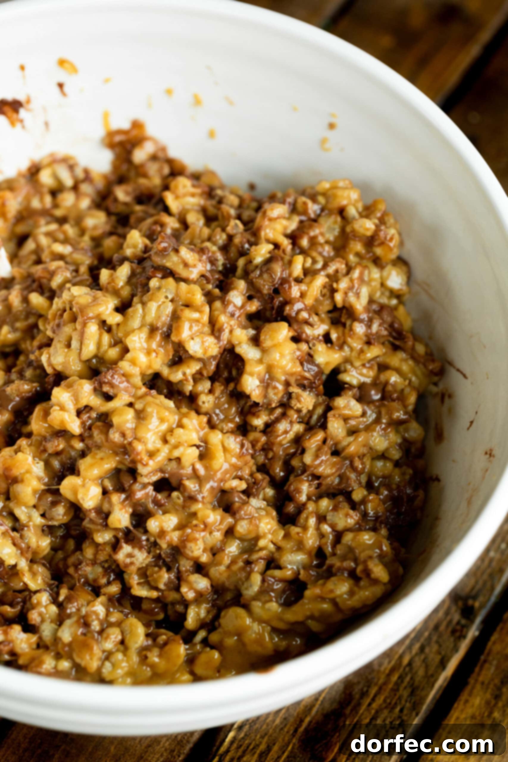 A photo of a white mixing bowl full of gooey rice krispies mixed with melting Reese's peanut butter cups, illustrating the texture.